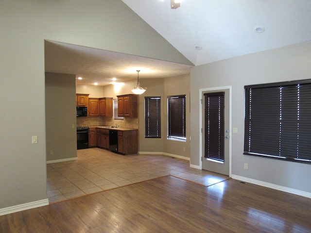 kitchen featuring decorative light fixtures, black appliances, lofted ceiling, and light hardwood / wood-style floors