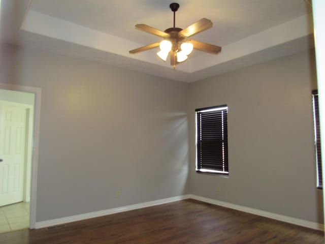 unfurnished room with dark hardwood / wood-style floors, ceiling fan, and a raised ceiling