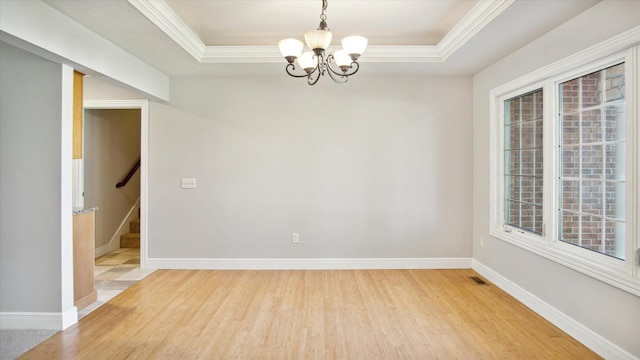 empty room with a tray ceiling, ornamental molding, a notable chandelier, and hardwood / wood-style flooring