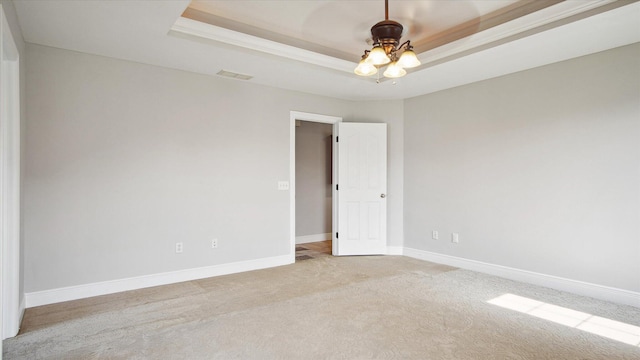 spare room with ceiling fan, a raised ceiling, and light carpet