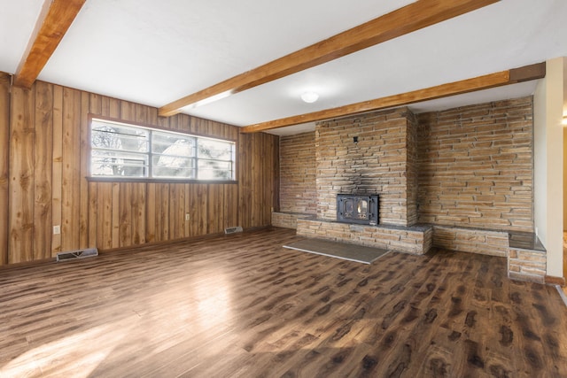 unfurnished living room featuring beam ceiling, wood-type flooring, a wood stove, and wooden walls