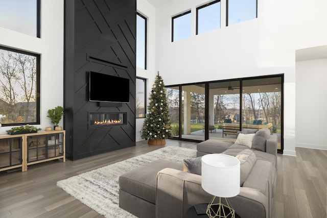 living room featuring ceiling fan, a fireplace, wood-type flooring, and a high ceiling