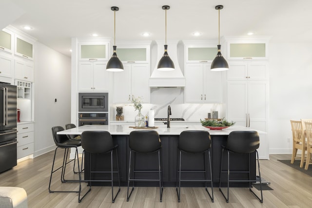 kitchen featuring light wood-type flooring, fridge, built in microwave, oven, and hanging light fixtures