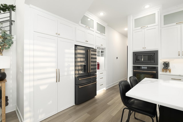 kitchen with white cabinets, hardwood / wood-style floors, a breakfast bar area, and black appliances