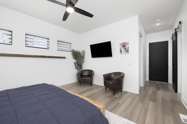 bedroom featuring hardwood / wood-style floors, a barn door, and ceiling fan