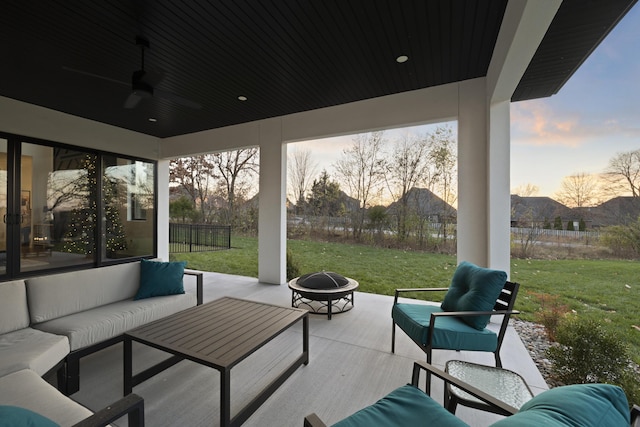 patio terrace at dusk with ceiling fan, a yard, and an outdoor living space with a fire pit