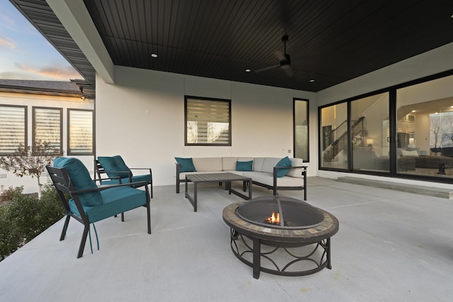 patio terrace at dusk featuring ceiling fan and an outdoor living space with a fire pit