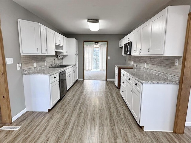 kitchen featuring light stone countertops, white cabinetry, sink, black appliances, and light wood-type flooring