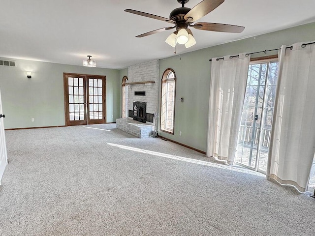 unfurnished living room with a brick fireplace, ceiling fan, light colored carpet, and french doors