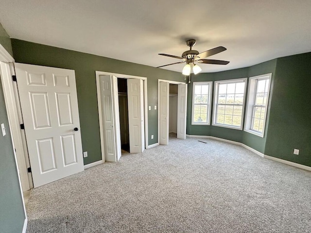 unfurnished bedroom with multiple closets, ceiling fan, and light colored carpet