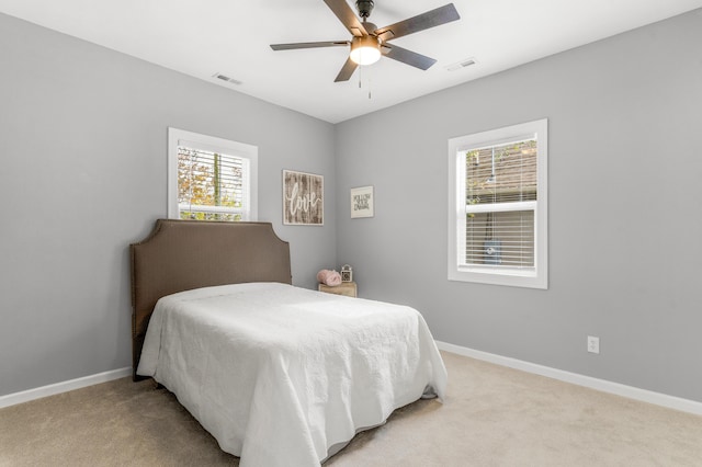 bedroom with ceiling fan, light colored carpet, and multiple windows