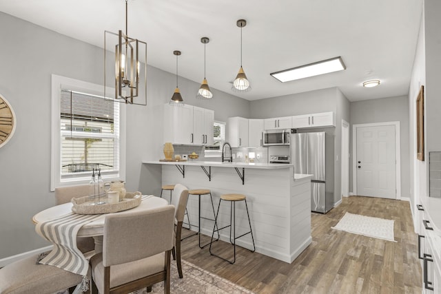 kitchen with white cabinetry, kitchen peninsula, wood-type flooring, a breakfast bar area, and appliances with stainless steel finishes