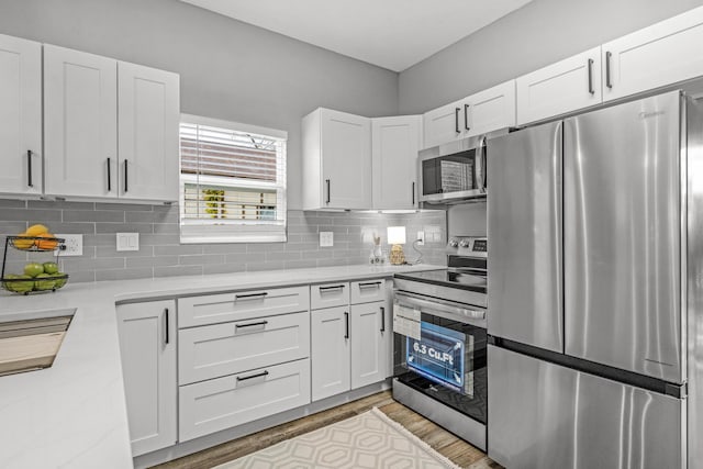 kitchen with backsplash, light hardwood / wood-style floors, white cabinetry, and stainless steel appliances