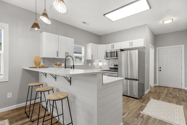 kitchen with kitchen peninsula, appliances with stainless steel finishes, a kitchen breakfast bar, white cabinets, and light hardwood / wood-style floors