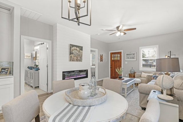 dining area with a large fireplace, light hardwood / wood-style flooring, and ceiling fan with notable chandelier