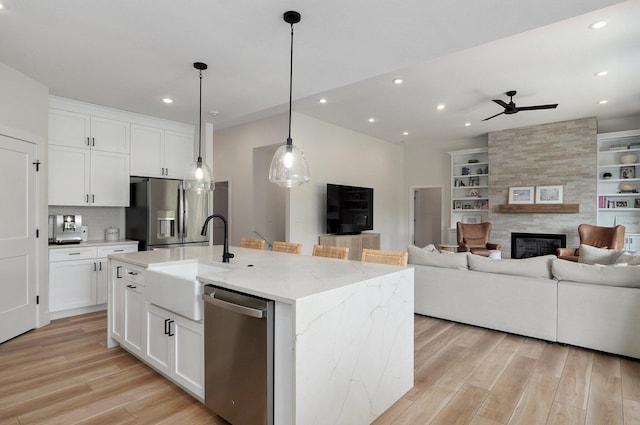 kitchen with white cabinetry, a large fireplace, light stone countertops, stainless steel appliances, and a center island with sink