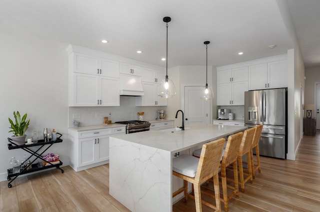 kitchen with light stone countertops, stainless steel appliances, a kitchen island with sink, light hardwood / wood-style flooring, and white cabinets