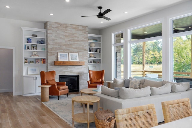 living room featuring a large fireplace, light hardwood / wood-style floors, built in features, and ceiling fan