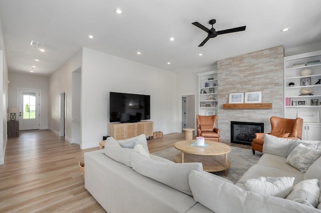 living room with a fireplace, built in shelves, light hardwood / wood-style flooring, and ceiling fan