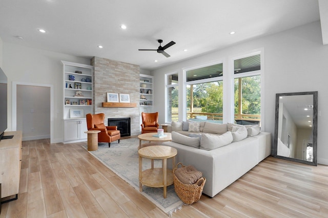 living room featuring a fireplace, light wood-type flooring, built in features, and ceiling fan