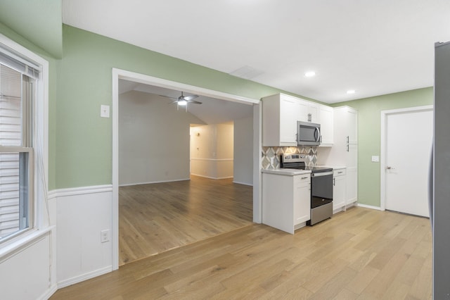 kitchen with decorative backsplash, appliances with stainless steel finishes, light wood-type flooring, ceiling fan, and white cabinetry