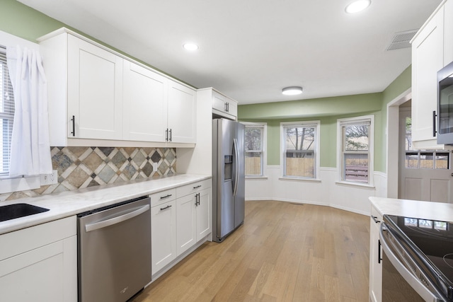 kitchen with white cabinets, appliances with stainless steel finishes, tasteful backsplash, and light hardwood / wood-style floors