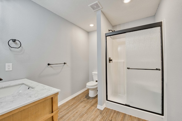 bathroom with toilet, vanity, a shower with shower door, and hardwood / wood-style flooring