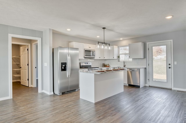 kitchen with hanging light fixtures, stainless steel appliances, a kitchen island, white cabinets, and hardwood / wood-style flooring