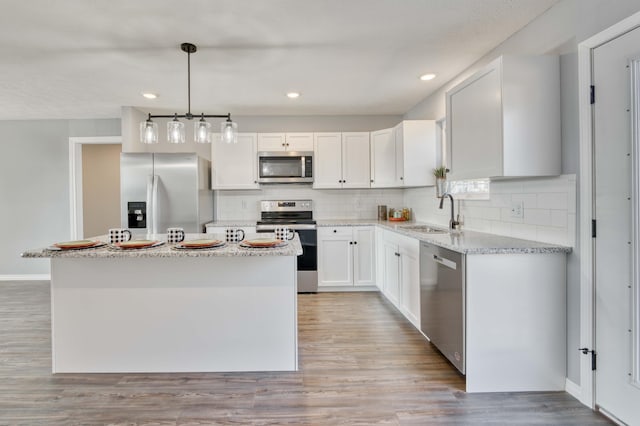 kitchen with appliances with stainless steel finishes, sink, decorative light fixtures, a center island, and white cabinetry