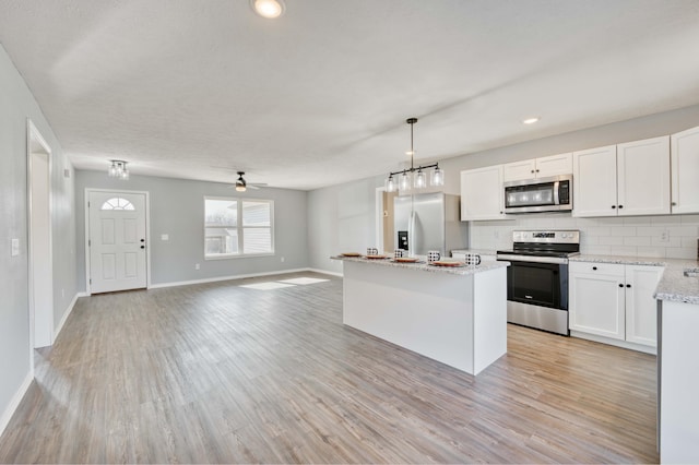 kitchen with decorative light fixtures, stainless steel appliances, white cabinetry, and light hardwood / wood-style flooring