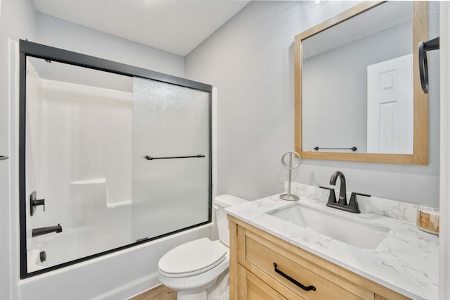 full bathroom featuring combined bath / shower with glass door, vanity, a textured ceiling, wood-type flooring, and toilet