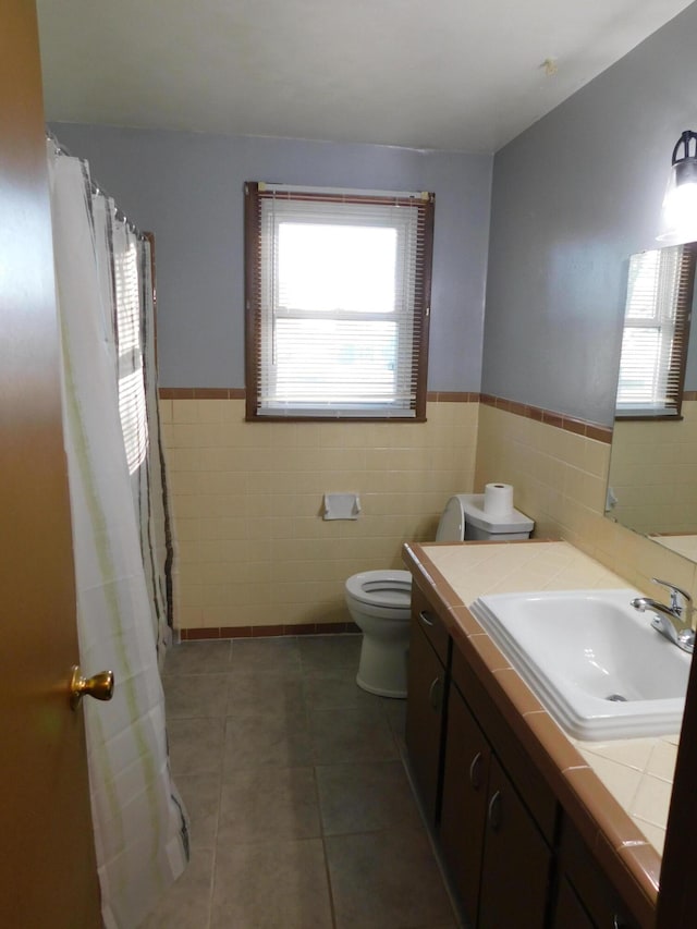 bathroom featuring toilet, tile patterned floors, tile walls, and a healthy amount of sunlight