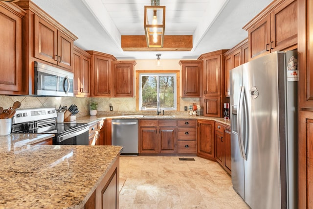 kitchen with light stone countertops, sink, stainless steel appliances, a raised ceiling, and tasteful backsplash
