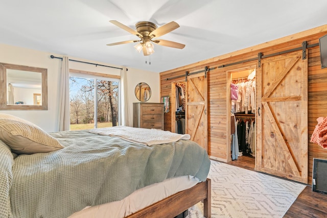 bedroom with ceiling fan, wooden walls, a barn door, a spacious closet, and a closet