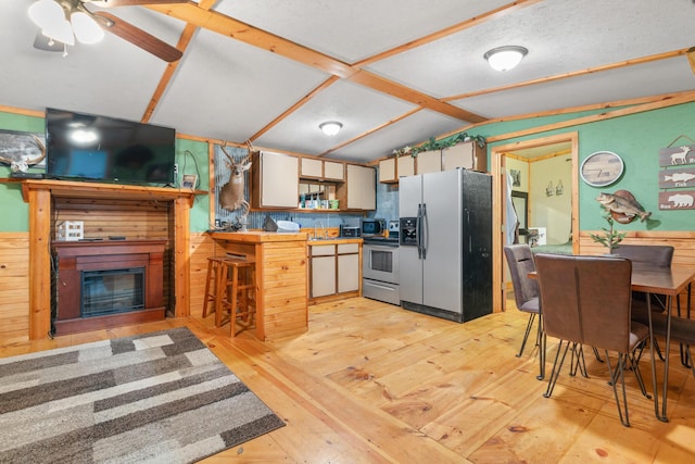 kitchen featuring wood walls, lofted ceiling, light hardwood / wood-style flooring, appliances with stainless steel finishes, and white cabinetry
