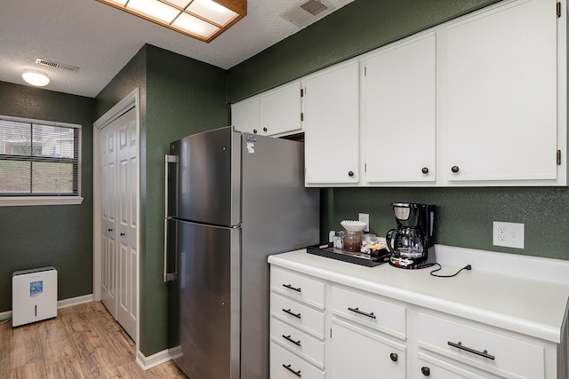 kitchen featuring white cabinets, stainless steel fridge, light hardwood / wood-style floors, and a textured ceiling