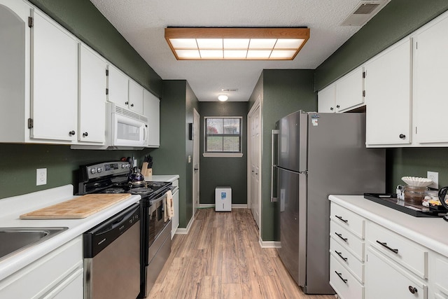 kitchen featuring white cabinets, a textured ceiling, stainless steel appliances, and light hardwood / wood-style flooring