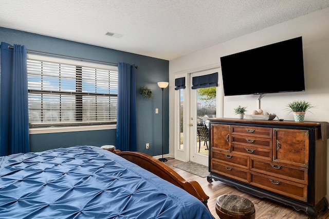 bedroom with access to exterior, wood-type flooring, and a textured ceiling