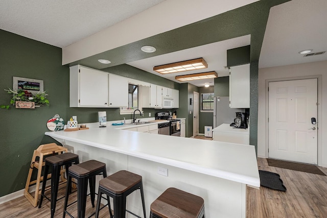 kitchen with light wood-type flooring, white cabinetry, kitchen peninsula, and stainless steel electric range oven