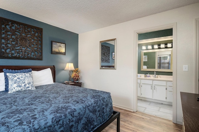 bedroom with ensuite bathroom, light hardwood / wood-style floors, sink, and a textured ceiling