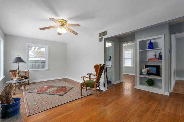 living area with hardwood / wood-style flooring, built in shelves, and ceiling fan