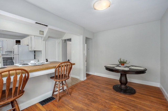 kitchen featuring a kitchen breakfast bar, dark hardwood / wood-style flooring, white fridge, white cabinetry, and kitchen peninsula