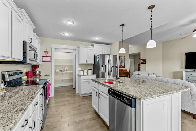 kitchen featuring decorative backsplash, appliances with stainless steel finishes, white cabinets, and a kitchen island with sink