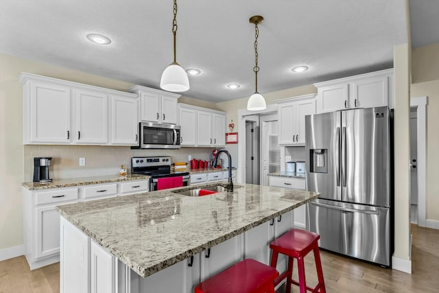 kitchen featuring a kitchen island with sink, white cabinetry, hanging light fixtures, and appliances with stainless steel finishes