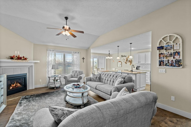 living room featuring ceiling fan, sink, dark hardwood / wood-style flooring, lofted ceiling, and a tiled fireplace