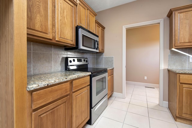 kitchen featuring decorative backsplash, light tile patterned floors, light stone countertops, and appliances with stainless steel finishes