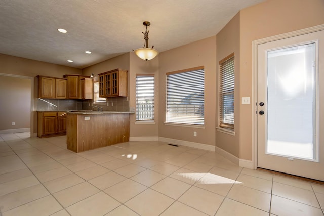 kitchen featuring kitchen peninsula, decorative backsplash, a textured ceiling, pendant lighting, and light tile patterned floors