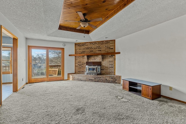 unfurnished living room with carpet, a wood stove, ceiling fan, a textured ceiling, and a tray ceiling