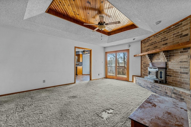 unfurnished living room with carpet flooring, a wood stove, ceiling fan, a raised ceiling, and a textured ceiling