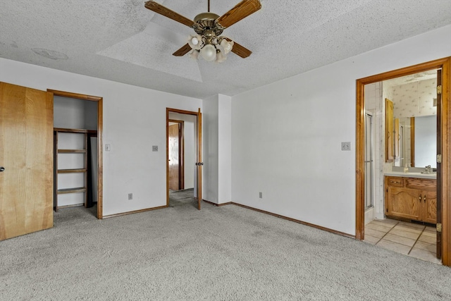 unfurnished bedroom with ceiling fan, light colored carpet, a textured ceiling, and connected bathroom